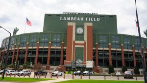 Exterior view of Lambeau Field, home of the Green Bay Packers, showcasing the iconic green and brick structure, American flag, and surrounding parking area.